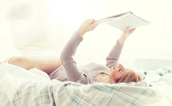 Evde yatakta kitap okuyan genç bir kadın. — Stok fotoğraf