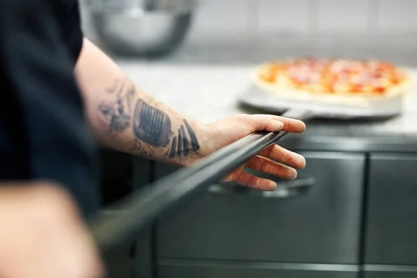 Cozinhar ou padeiro mão com pizza na casca na pizzaria — Fotografia de Stock