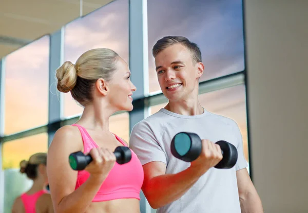 Smiling young woman with personal trainer in gym — Stock Photo, Image