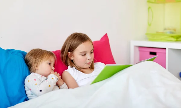 Meninas ou irmãs lendo livro na cama — Fotografia de Stock