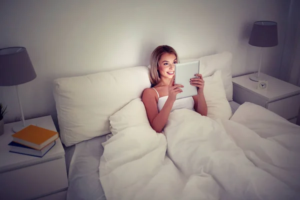 Счастливая молодая женщина с планшетным компьютером в постели дома — стоковое фото