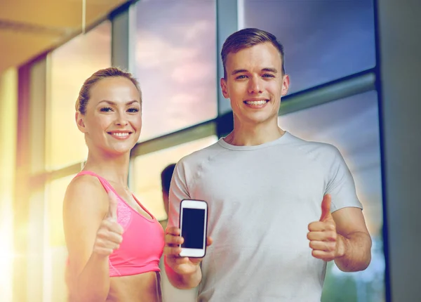 Smiling young woman with personal trainer in gym — Stock Photo, Image