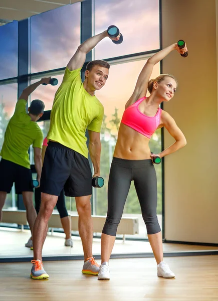 Uomo e donna sorridente con manubri in palestra — Foto Stock