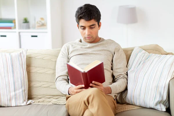 Homem sentado no sofá e livro de leitura em casa — Fotografia de Stock