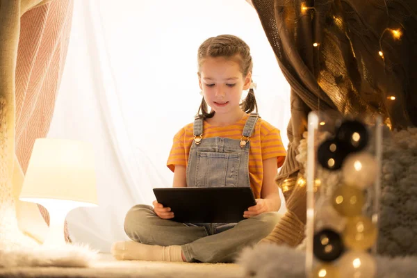 Маленькая девочка с планшетным ПК в детской палатке дома — стоковое фото