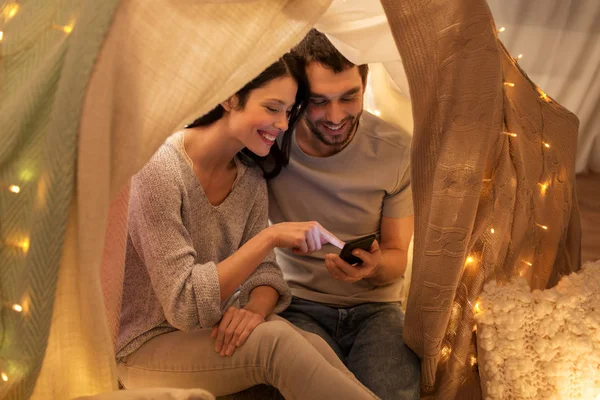 Feliz pareja con smartphone en tienda de campaña para niños en casa — Foto de Stock