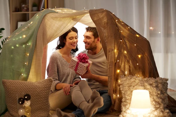 Happy couple with gift box in kids tent at home — Stock Photo, Image