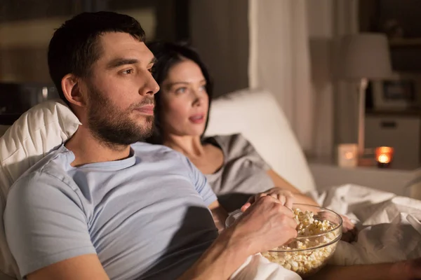 couple with popcorn watching tv at night at home