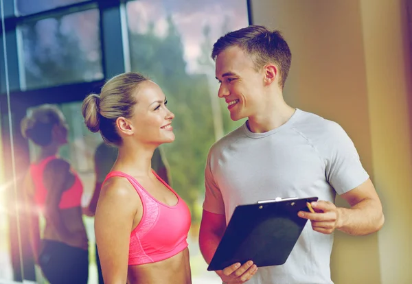 Giovane donna sorridente con personal trainer in palestra — Foto Stock