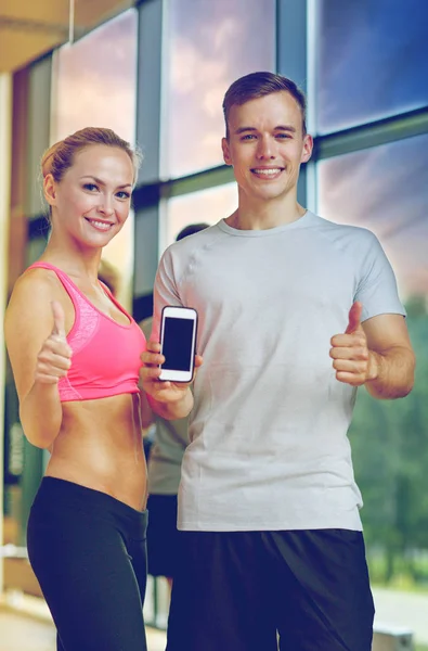 Spor salonunda kişisel antrenörüyle gülümseyen genç bir kadın. — Stok fotoğraf