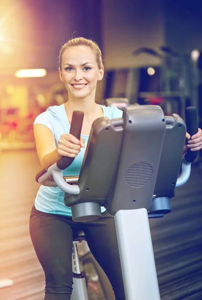 Smilende kvinne som trener på treningssykkel i gymsalen – stockfoto