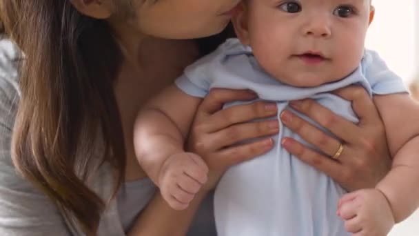 Счастливая молодая мать целует маленького ребенка дома — стоковое видео