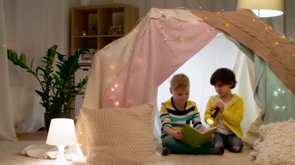 Niños felices leyendo libro en tienda de campaña de los niños en casa — Vídeos de Stock