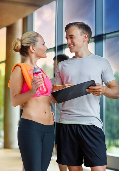 Giovane donna sorridente con personal trainer in palestra — Foto Stock