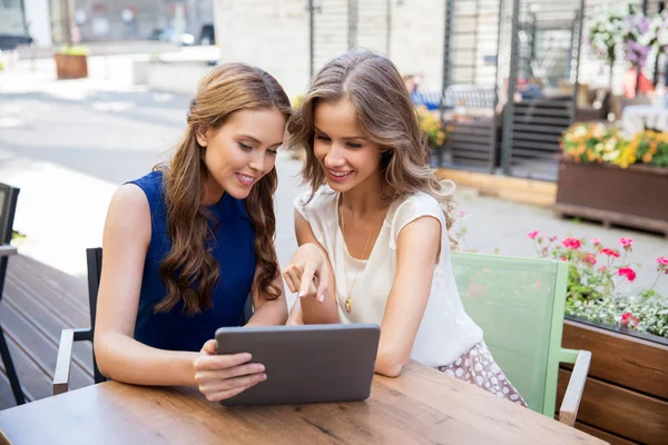 Счастливые молодые женщины с планшетным компьютером в открытом кафе — стоковое фото