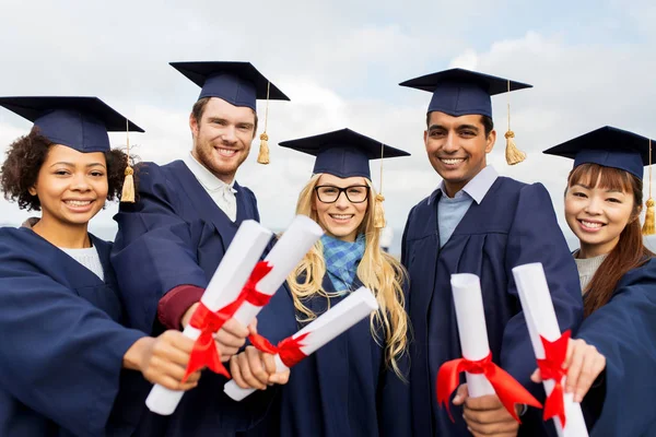 Happy students in mortar boards with diplomas — Stock Photo, Image