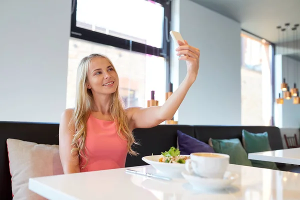 Kvinna med smartphone tar selfie på restaurang — Stockfoto