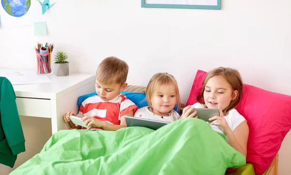 Дети с планшетным ПК и смартфоны в постели дома — стоковое фото