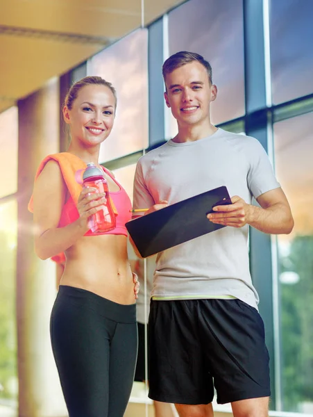 Smiling young woman with personal trainer in gym — Stock Photo, Image