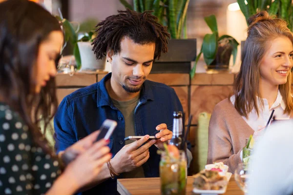 Друзья со смартфонами едят в ресторане — стоковое фото