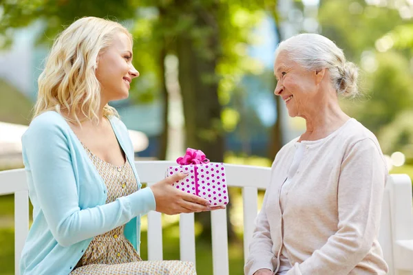 Daughter giving present to senior mother at park — Stock Photo, Image