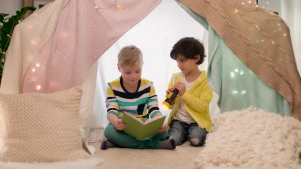 Niños felices leyendo libro en tienda de campaña de los niños en casa — Vídeos de Stock