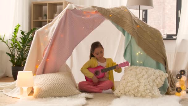 Девушка с игрушечной гитарой играет в детской палатке дома — стоковое видео