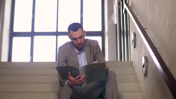 Бизнесмен с папкой, сидящий на лестнице — стоковое видео