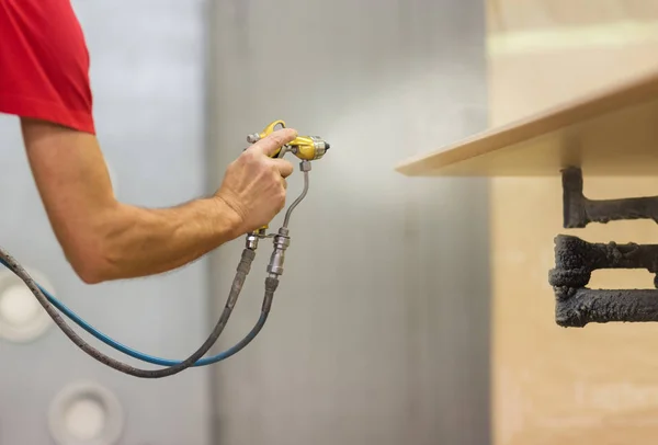 Worker hand sprays urethane finish to board — Stock Photo, Image