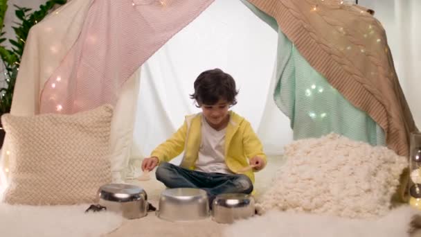 Мальчик с горшками играет музыку в детской палатке дома — стоковое видео