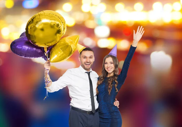 Casal feliz com tampas de festa e balões — Fotografia de Stock