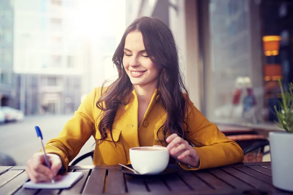 Щаслива жінка з блокнотом п'є какао в кафе — стокове фото