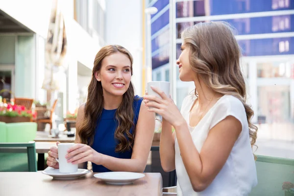 Улыбающиеся молодые женщины пьют кофе в уличном кафе — стоковое фото