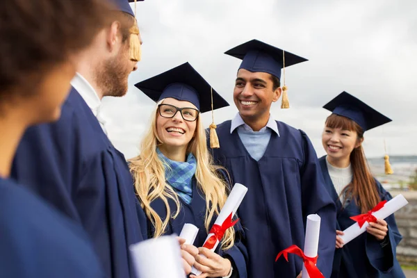 Happy students in mortar boards with diplomas — Stock Photo, Image