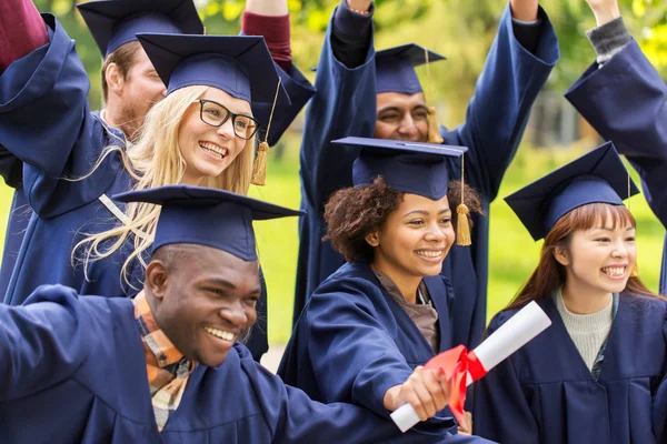 Happy students in mortar boards with diplomas — Stock Photo, Image