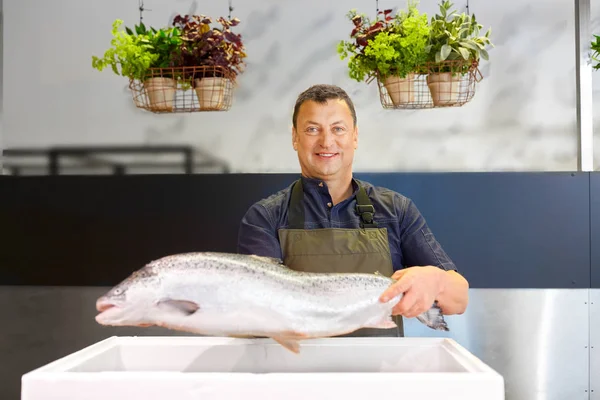 Vendedor varón feliz celebración de la trucha en la tienda de pescado — Foto de Stock