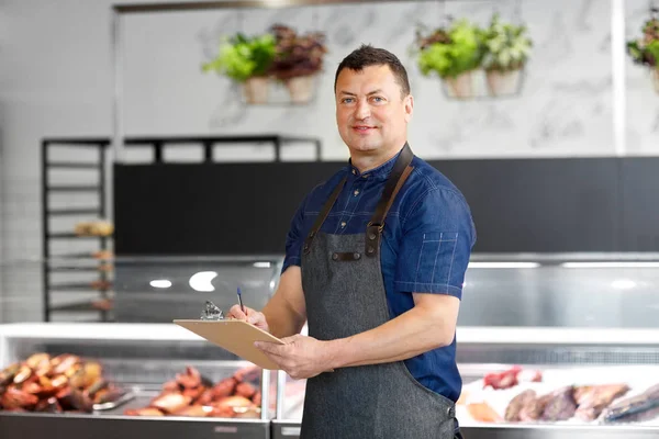 Seller at fish shop writing to clipboard — Stock Photo, Image