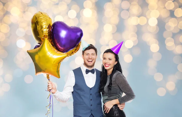 Echtpaar met partij caps en ballonnen over verlichting — Stockfoto