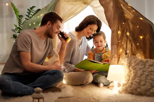 Libro de lectura familiar feliz en tienda de campaña para niños en casa —  Fotos de Stock