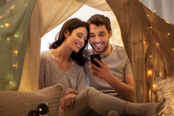 Glückliches Paar mit Smartphone im Kinderzelt zu Hause — Stockfoto