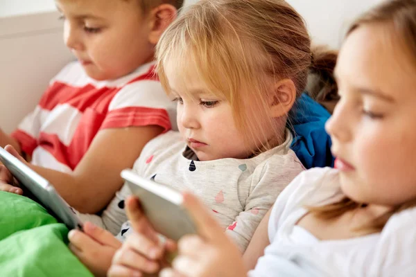 Kids with tablet pc and smartphone in bed at home — Stock Photo, Image