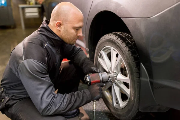 Mecânico automático com chave de fenda trocando pneu do carro — Fotografia de Stock