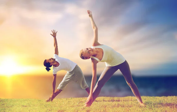 Paar maken yoga driehoek pose buitenshuis — Stockfoto