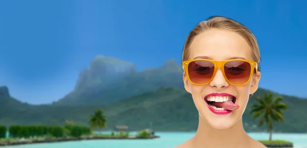Frau in Schattierungen zeigt Zunge über Sommerstrand — Stockfoto