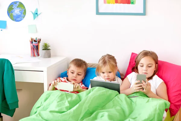 Дети с планшетным ПК и смартфоны в постели дома — стоковое фото