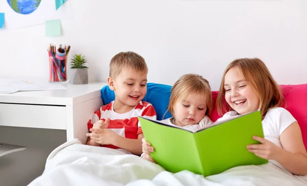 Crianças lendo livro na cama em casa — Fotografia de Stock