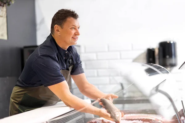 Male seller showing seafood at fish shop fridge — Stock Photo, Image