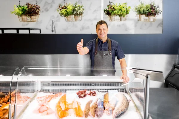 Продавець морепродуктів у рибному магазині, що показує великі пальці вгору — стокове фото