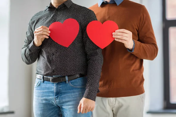 Close up de feliz casal masculino segurando corações vermelhos — Fotografia de Stock