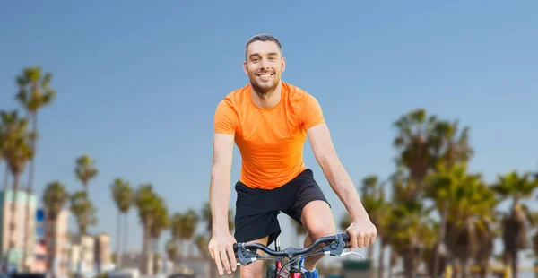 Happy young man riding bicycle over venice beach — Stock Photo, Image